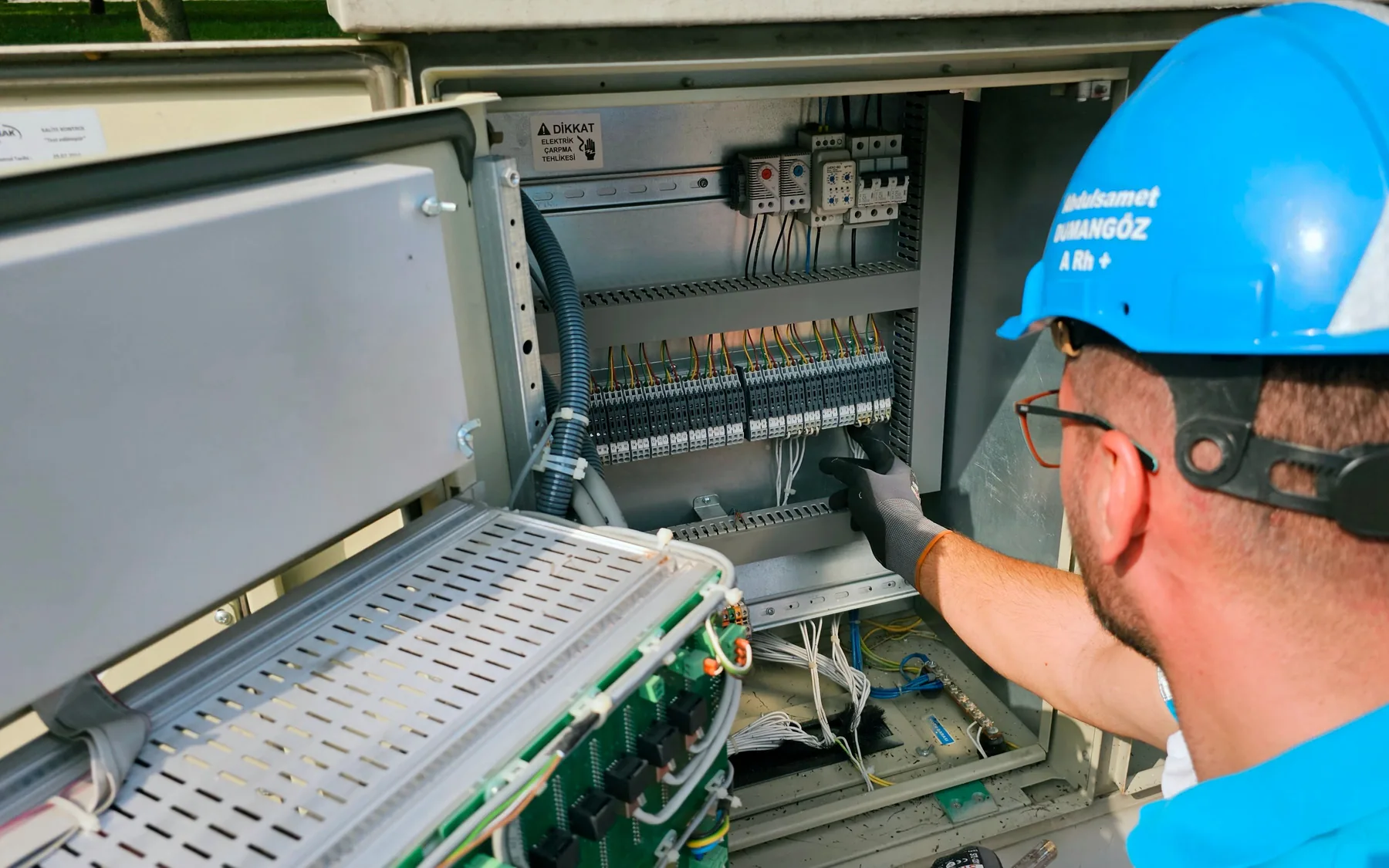 Electricista con casco y guantes revisando un cuadro de control eléctrico